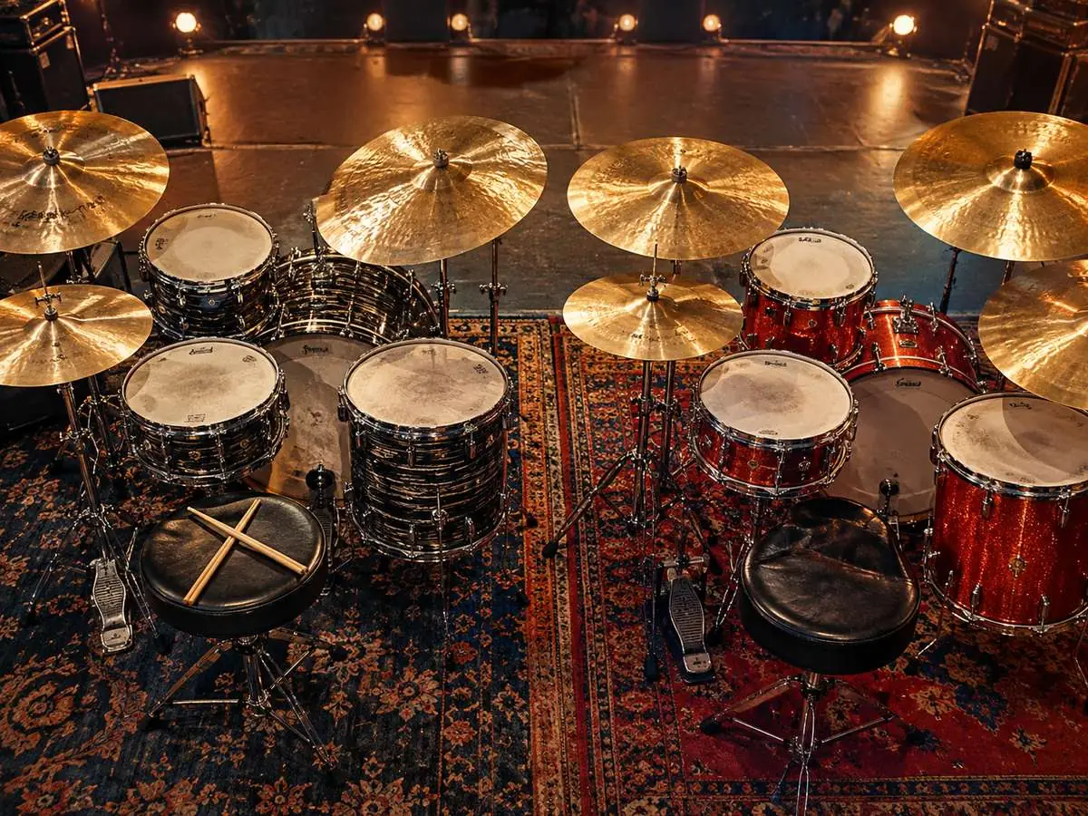 Two drum kits set up side by side on a concert stage under warm lights